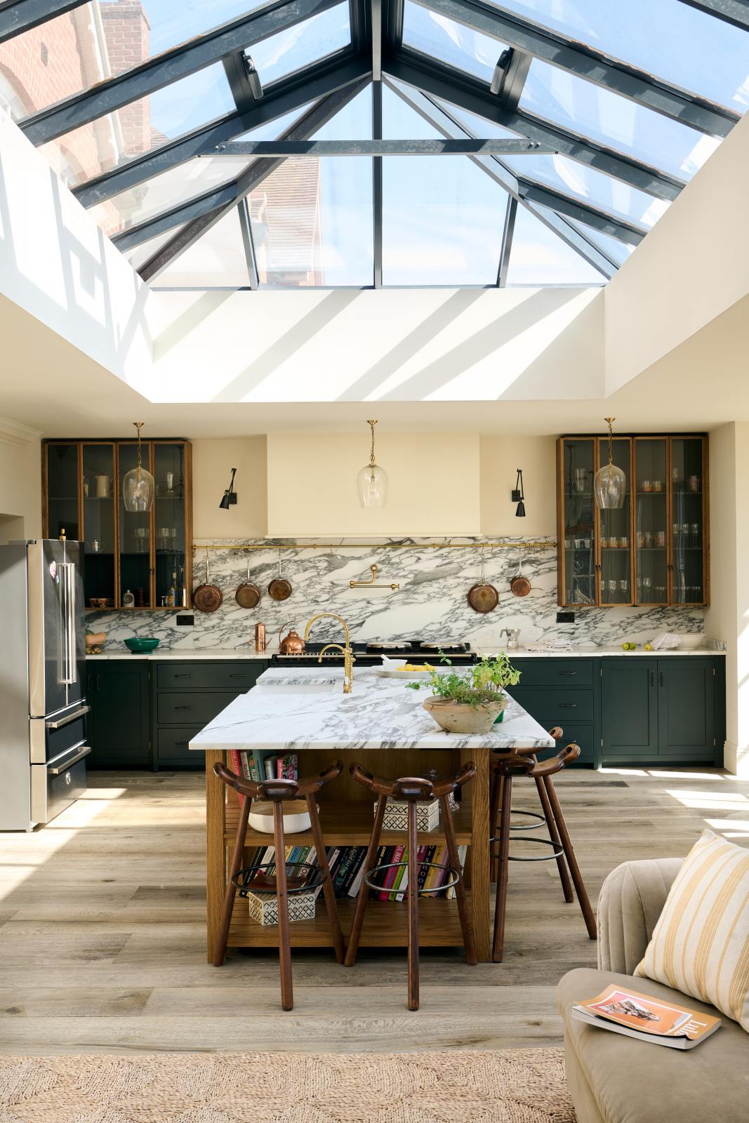 A closer look at an elegant and spacious Haberdasher’s kitchen features a large cooker run, a kitchen island with a double Belfast sink, an aged brass Ionian tap, an Arabescato marble worktop, splashback, and glazed cupboards. Adorned with vintage furniture, artisan ceramics, glass flower pendant lights, lemons, and a large skylight, this kitchen creates a classic social space with functional storage.
