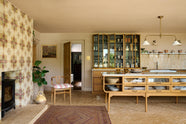 A warm and chic Haberdasher’s kitchen features an L-shaped sink and cooker run, countertop cupboards, a kitchen island, a Carrara and copper mix worktop, and a double-fluted marble sink. Adorned with artisan ceramics, a deVOL gaselier light, Heirloom wall lights, large vintage rugs, and luscious green house plants, this kitchen creates a warm and inviting Spanish-inspired space in Yorkshire.