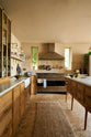 Nestled between a warm and chic Haberdasher’s kitchen features an L-shaped sink and cooker run, countertop cupboards, a kitchen island, a Carrara and copper mix worktop, and a double-fluted marble sink, is a large stainless steel gas cooker with a matching canopy. Adorned with artisan ceramics, Heirloom wall lights, a large vintage rug, and luscious green house plants, this kitchen creates a warm and inviting Spanish-inspired space in Yorkshire.