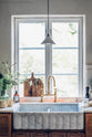 A closer look at a warm and inviting Haberdasher’s kitchen featuring a sink run with a Carrara marble worktop, a double-fluted marble sink, an aged brass Ionian tap, and prep tables with a copper worktop. Beautifully decorated with vintage items, artisan ceramics, wooden chopping boards, and a wild flower arrangement, this kitchen creates an airy and cosy Scandinavian small fishing town hideaway.