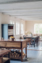 A warm and inviting Haberdasher’s kitchen features prep tables with a copper worktop. Beautifully decorated with vintage furniture and items, artisan ceramics, firewood, a bowl of lemons, a large couch, this space creates an airy and cosy Scandinavian small fishing town hideaway.