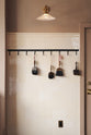 A tall cream subway-tile and border-tile splashback with an iron hook rack holding vintage paint brushes and an heirloom task light with a milk-glass shade.
