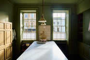 A quaint and stylish Wilkes green Heirloom kitchen features a large dairy table. Adorned with an aged brass pot filler, artisan ceramics, Heirloom gaselier lights, and cream subway splashback tiles, this kitchen creates a luxurious dining and social space.