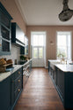 The room, a grand Georgian space from the 18th century, features charming pink walls. It showcases a modern Clerkenwell Blue shaker kitchen equipped with glazed wall cupboards, a shaker-style canopy, a cooker run, and a spacious kitchen island with a sink and an Arabescato marble worktop. The kitchen offers views of the balcony and garden through its original wooden floors and doors, and the renovated space complements the esteemed property beautifully.