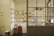 A simple Quaker cream and Folgate green Shaker scullery features architectural glazed partitions, bespoke shelving, and a sink run with a Silestone worktop, finished a cream subway tiles splashback. Lovingly adorned with artisan ceramics, wooden chopping boards, and antique kitchen accessories and furniture, it gives a sombre and practical space.