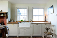 A closer look at the small and quaint mushroom-coloured Shaker kitchen’s features a sink run with a double Belfast sink, stave hardwood worktop, and an antique silver Ionian tap. Beautifully decorated with vintage furniture such as a large solid oak table, a silver scale, and assorted bric-a-brac, it creates a lovely social space full of character.