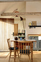 A small and humble pantry-blue Shaker kitchen features an L-shaped sink and cooker run with a stave hardwood worktop, a single Belfast sink, and aged brass Mayan taps. Beautifully decorated with a taxidermy bird sitting on the roof’s wooden beams, vintage furniture, books, and assorted bric-a-brac, creates a heartwarming family farm kitchen space.