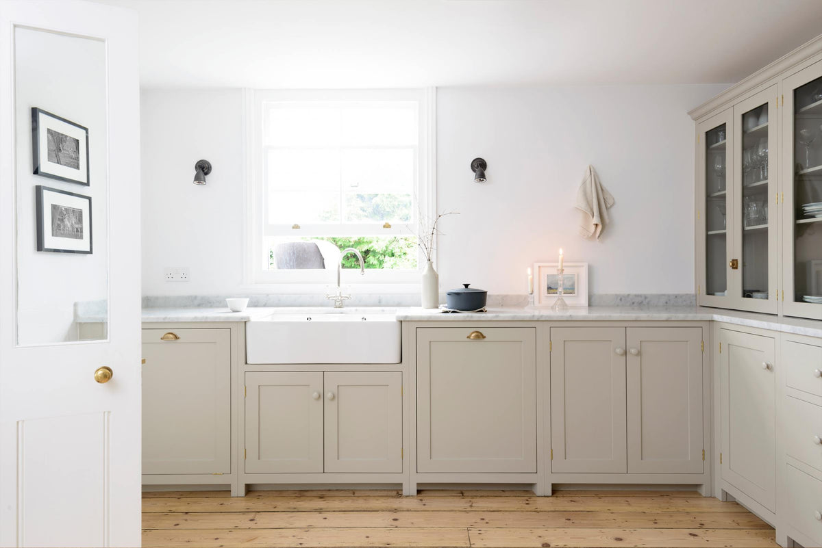 A simple mushroom-coloured shaker kitchen features a marble worktop, a double Belfast sink with an antique silver Ionian tap, and glazed cabinets.