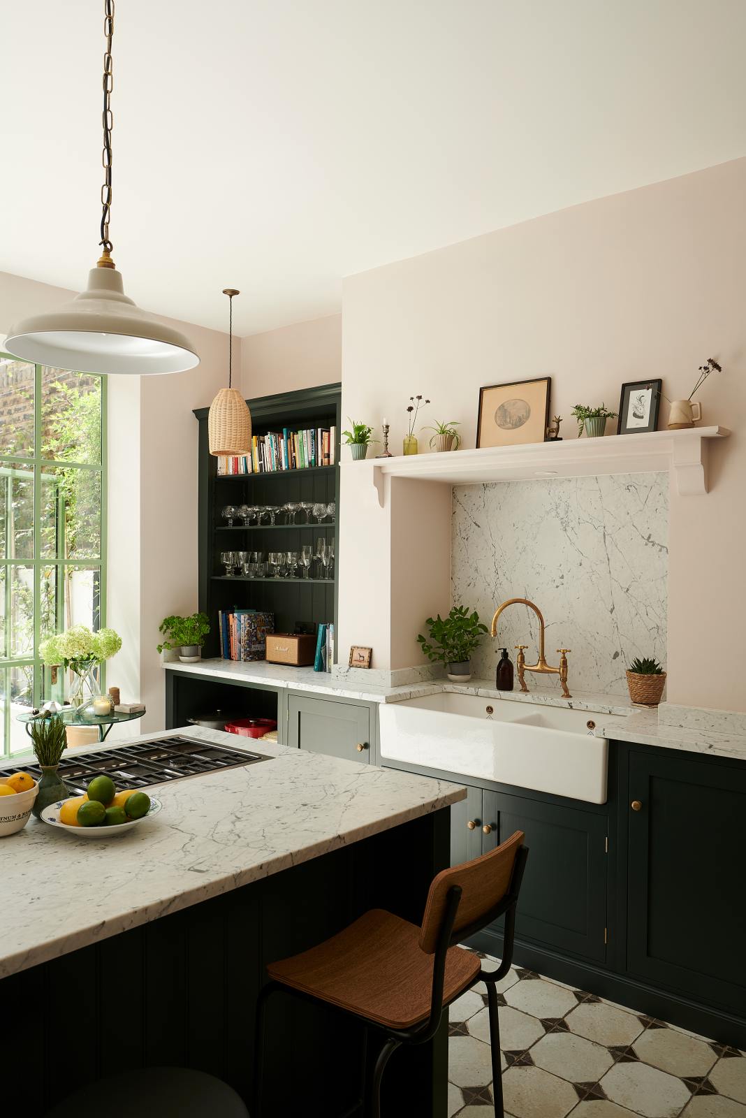An angled view of the Bakehouse Green shaker kitchen’s cooker kitchen island and sink run features a marble worktop, open cabinets and shelves, along with a double Belfast sink, an aged brass Ionian tap, and a Carrara marble splashback.