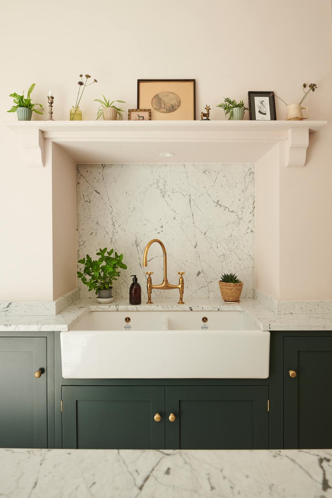 A close-up view of the Bakehouse Green shaker kitchen features a double Belfast sink, an aged brass Ionian tap, and a Carrara marble splashback set within the concave of the chimney.