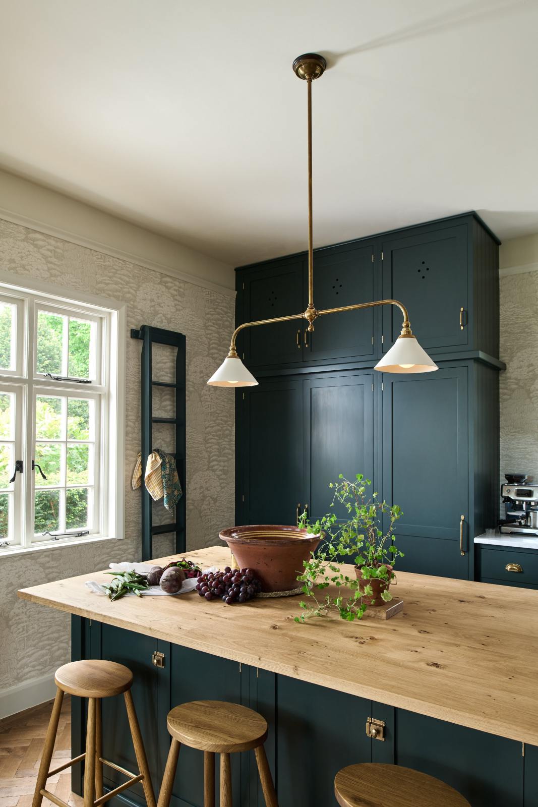A closer look at the double Belfast sink with an aged brass Ionian tap in the Bakehouse Green shaker kitchen’s sink run, featuring Carrara marble worktop. At the nook are the Emerald Green London tiles, which add colour to the off-white, delicately patterned wallpaper.