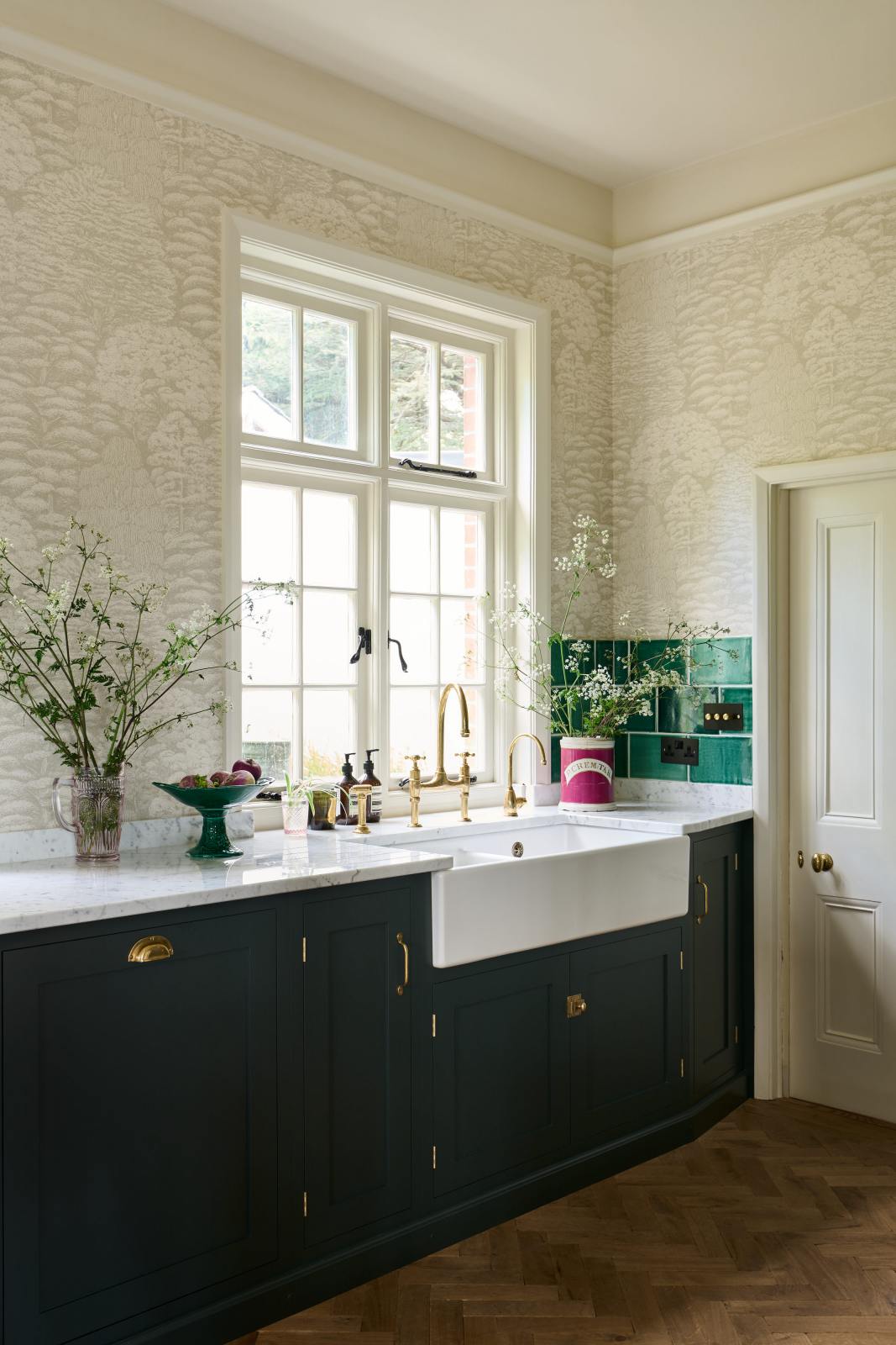 A closer look at the double Belfast sink with an aged brass Ionian tap in the Bakehouse Green shaker kitchen’s sink run, featuring Carrara marble worktop. At the nook are the Emerald Green London tiles, which add colour to the off-white, delicately patterned wallpaper.