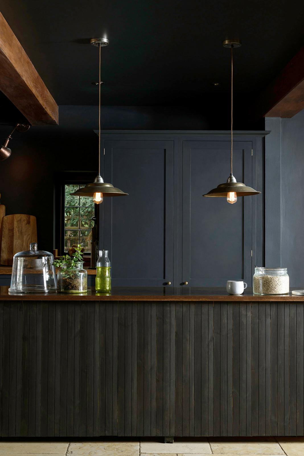 A closer look at the Pantry Blue, vintage kitchen island topped with Iroko wood. Light stone flooring enhances the space, featuring wooden ceiling accents, a large cooker splashback, and two hanging lights above the island.
