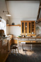 A scullery yellow shaker kitchen with a small sink run with a Carrara marble sink, a full-height cabinet, shaker shelves and a shaker bench seat. The kitchen features a single Belfast sink with aged brass Mayan taps, a collection of vintage furniture and beloved items.