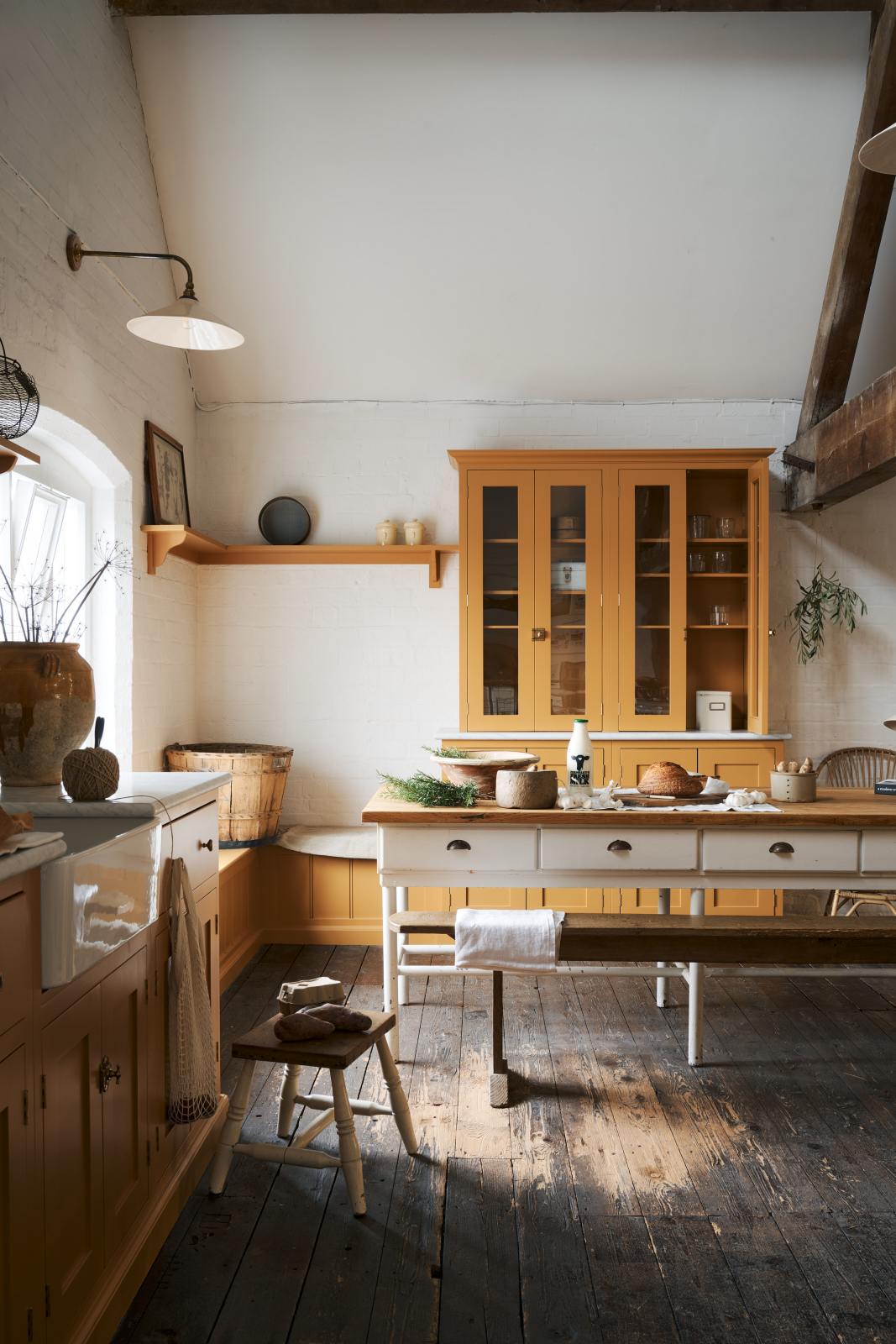 A scullery yellow shaker kitchen with a small sink run with a Carrara marble sink, a full-height cabinet, shaker shelves and a shaker bench seat. The kitchen features a single Belfast sink with aged brass Mayan taps, a collection of vintage furniture and beloved items.