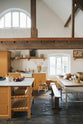 A scullery yellow shaker kitchen with a small sink run with a Carrara marble sink, a full-height cabinet, shaker shelves, an L-shaped shaker bench seat and a closed larder with glazed cupboards. The kitchen features a single Belfast sink with aged brass Mayan taps, a collection of vintage furniture and beloved items such as mixing bowls and fresh produce. The ceilings are high and retain their original exposed wooden structure.