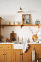 A close-up of the Scullery Yellow Shaker kitchen’s small sink run with a Carrara marble sink and Shaker shelves. It features a single Belfast sink with aged brass Mayan taps and displays vintage furniture alongside cherished items like mixing bowls and fresh produce.