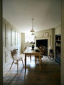 Looking through the archway in the kitchen, beside a large wooden shelf displaying a thoughtful selection of muted ceramics and mugs, the dining room comes into view with a pale wooden dining table and matching chairs.