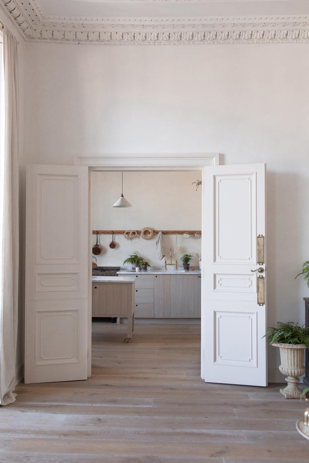 A peek into a warm and natural Sebastian Cox kitchen past beautiful high ceilings, an original intricate cornice, and a grand double-door entrance.