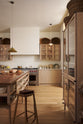 An all-natural and functional Sebastian Cox kitchen features a cooker and sink run with a marble worktop, glazed wall cupboards, a free-standing pantry with glazed doors and an iconic Haberdasher’s prep table with a copper worktop. Lovingly adorned with antiques, artisan ceramics, woven baskets, and beautiful houseplants, it creates a wonderfully simple kitchen with a love of natural sustainability.