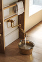A close-up of an all-natural and functional Sebastian Cox kitchen features an aged brass pot filler tap and a tall Haberdasher’s hanging rack. Lovingly adorned with a tea towel and a brass pan for a makeshift dog bowl.