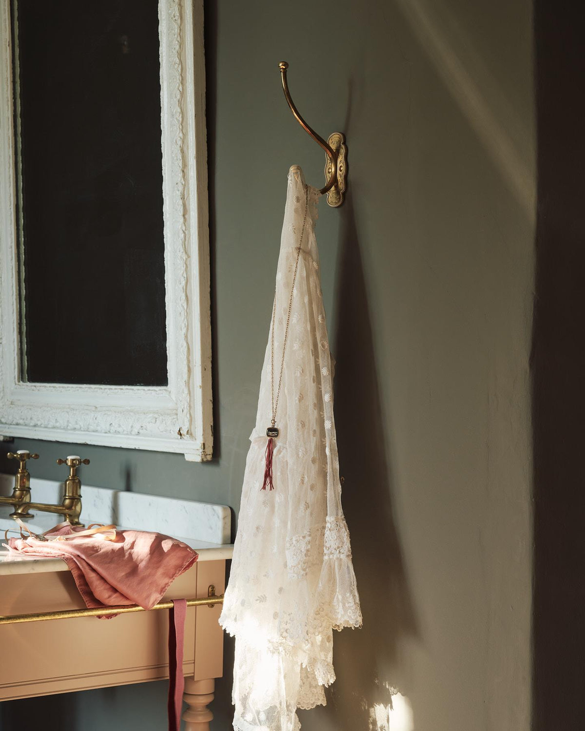 A large Parisian café-style brass hook, fitted to a grey painted wall with a lovely vintage laced fabric and necklace draped on it. TEST