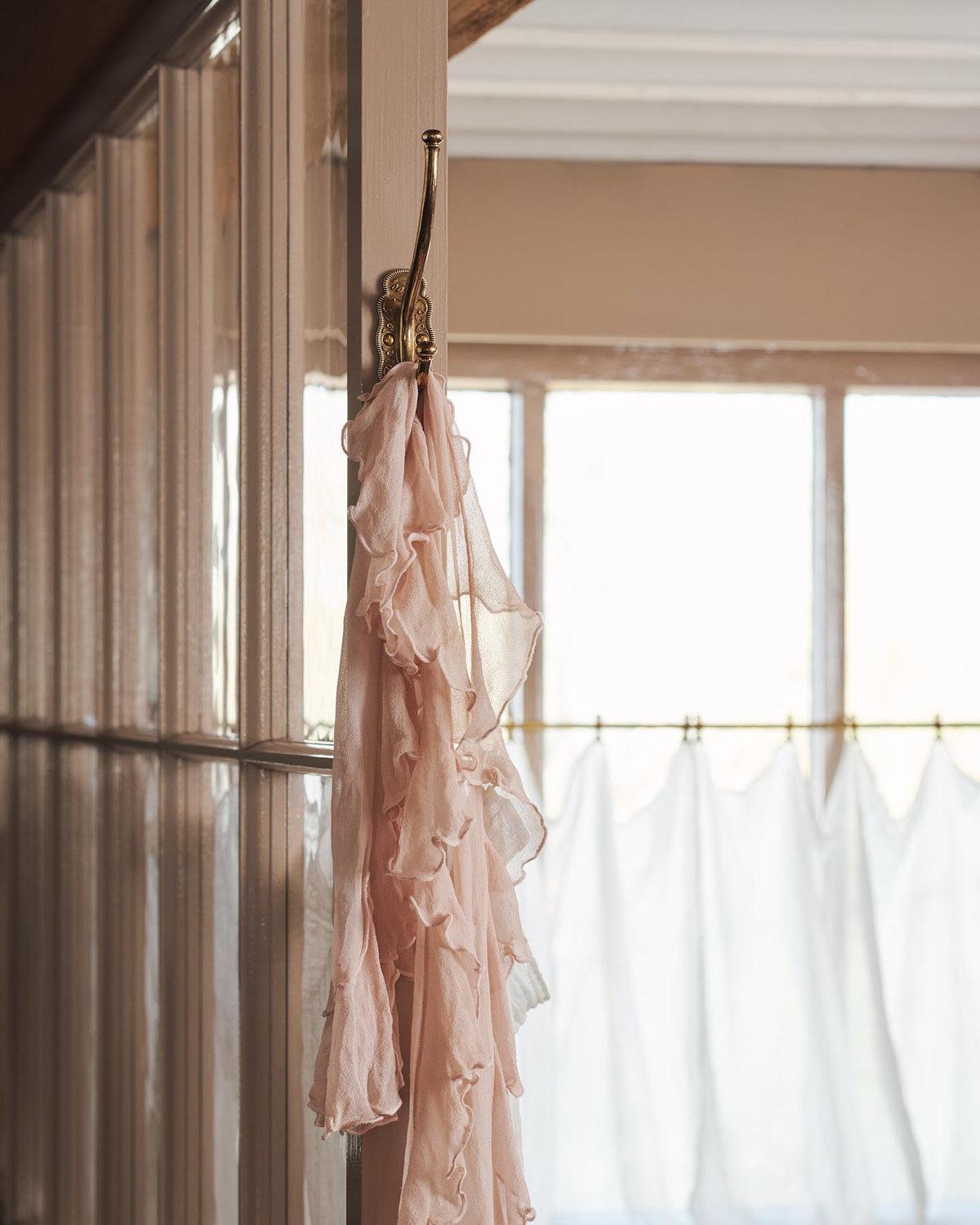 A small Parisian café-style brass hook, fitted to the frame of a pink painted glazed partition with a lovely pink frilled scarf draped on it. TEST
