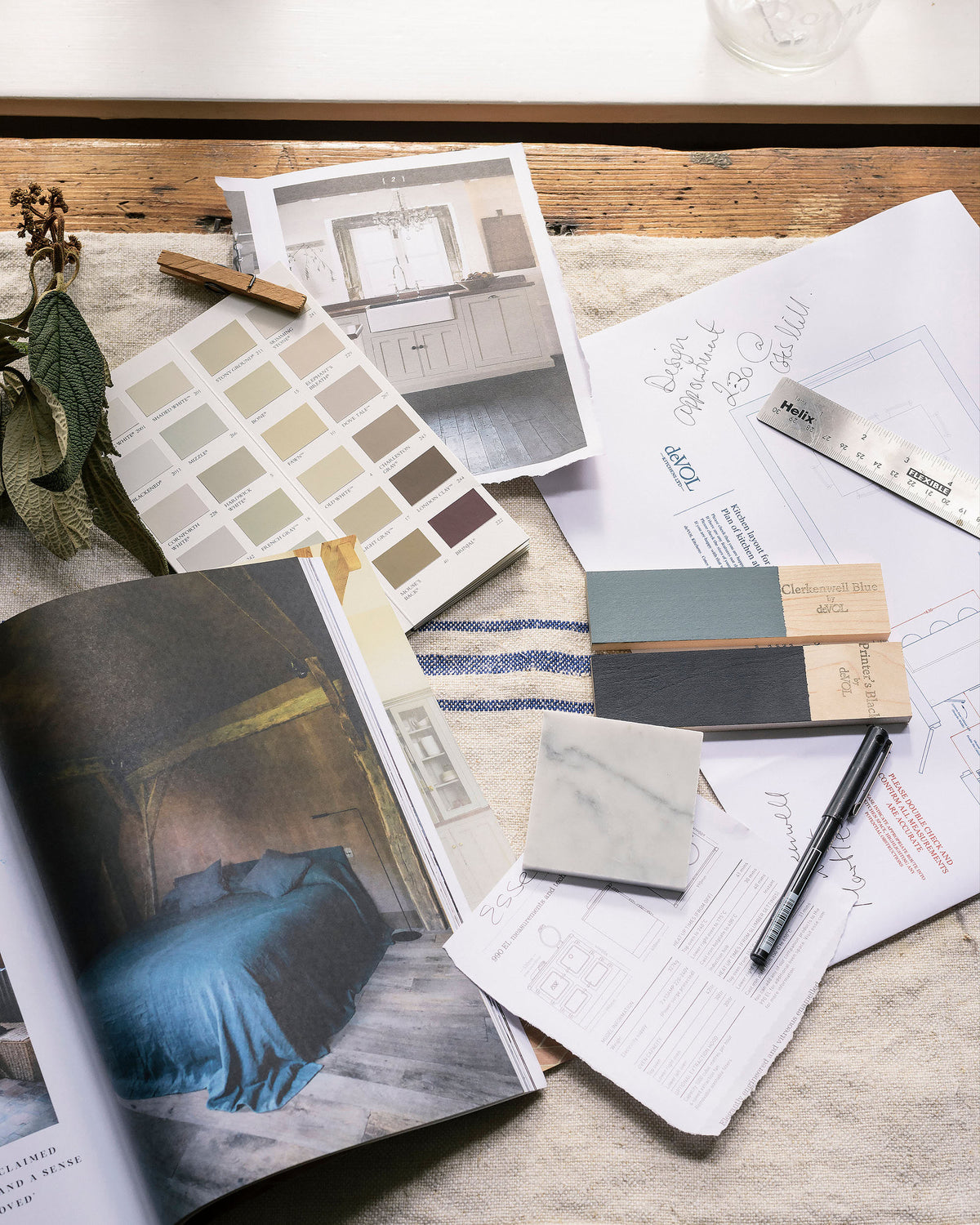 A table filled with design elements from sample colours, a detailed floor plan, tile samples, a ruler, pen and a brochure.