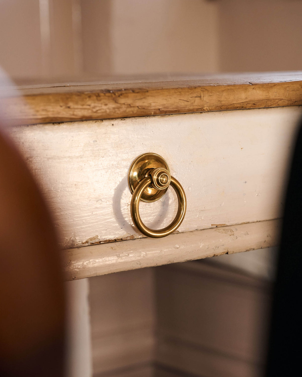 An oblique view of a Victorian-inspired ring pull handle in a warm burnished brass finish, fitted to the drawer of a small antique dining table.