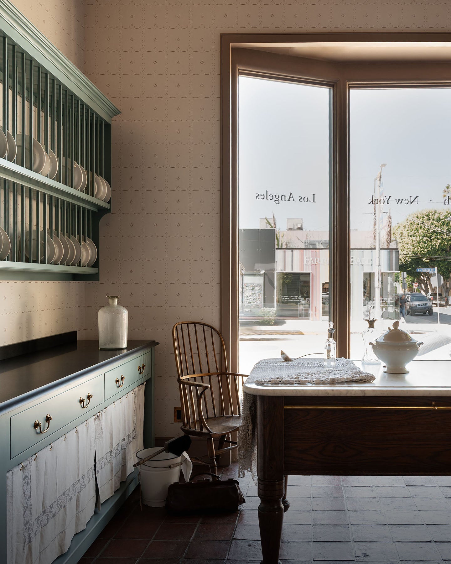A grand and spacious Heirloom kitchen with Trinity blue open cabinets and plate racks, Heirloom Dairy Tables, an Heirloom Gaselier light reaching all the way to the top of the high ceiling and rustic Square Terracotta tiles. Beautifully decorated with vintage furniture, artisan ceramics and .