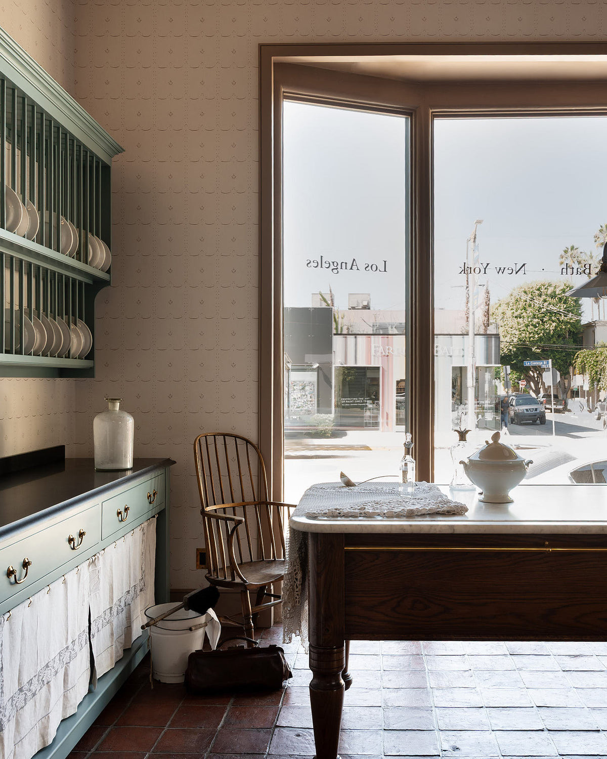 A grand and spacious Heirloom kitchen with Trinity blue open cabinets and plate racks, Heirloom Dairy Tables, an Heirloom Gaselier light reaching all the way to the top of the high ceiling and rustic Square Terracotta tiles. Beautifully decorated with vintage furniture, artisan ceramics and .