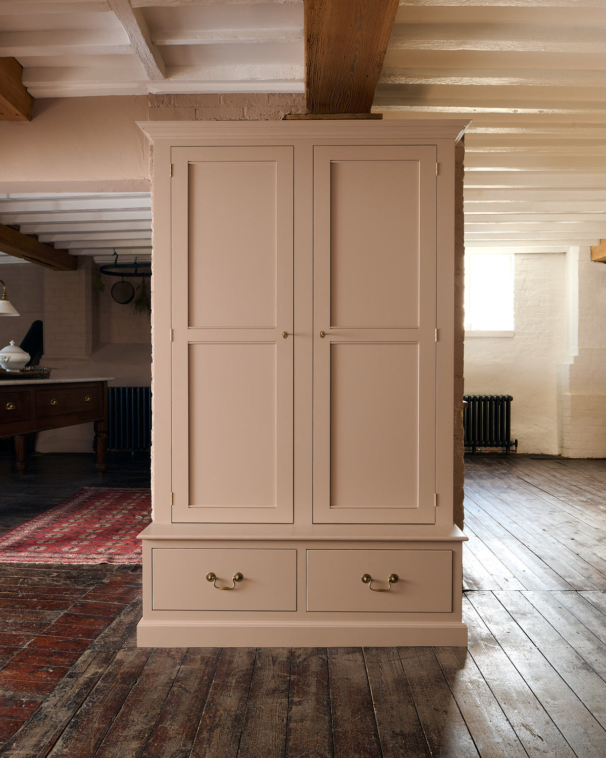 A Victorian-style pantry cupboard, painted inside and out in a soft pink colour. A pedestal base contains two box drawers with Georgian-style brass pull handles.