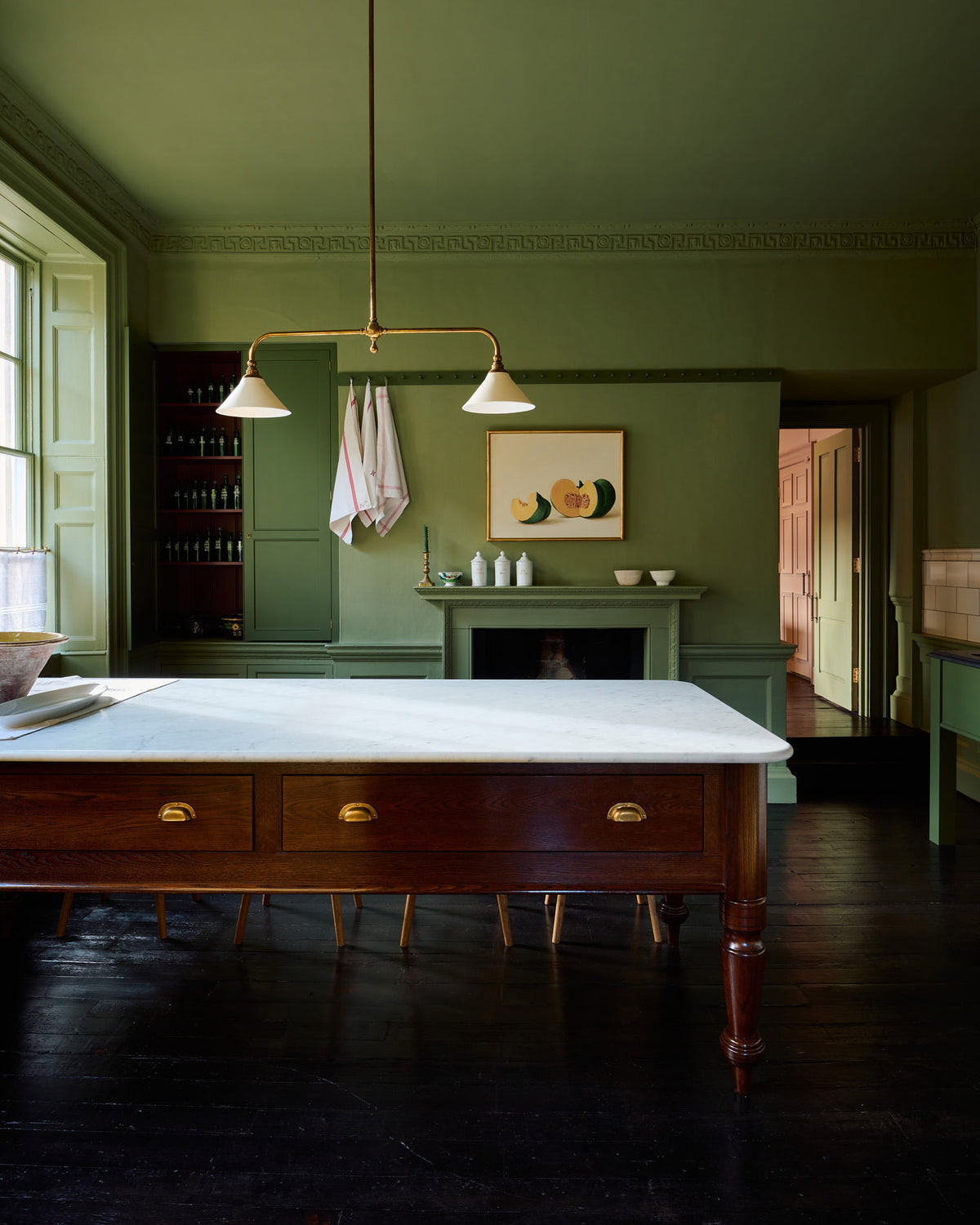 A quaint and stylish Wilkes green Heirloom kitchen features a sink cabinet, large plate rack, and dairy table. Adorned with an aged brass pot filler, artisan ceramics, Heirloom gaselier lights, cream subway splash back tiles, and a golden-framed sliced green pumpkin, this kitchen creates a luxurious dining and social space.