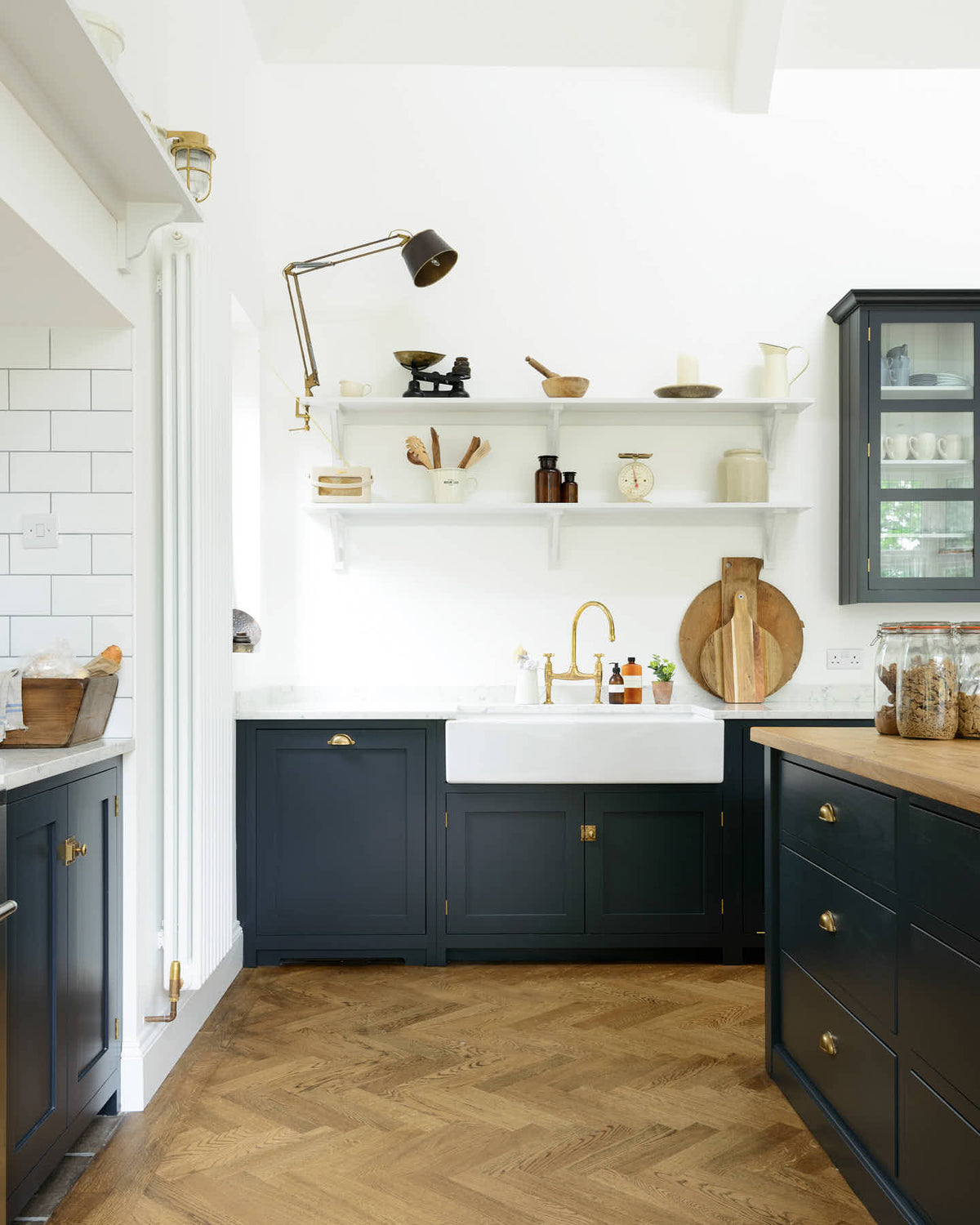 Looking at the pantry blue’s sink run with silestone worktop and the double Belfast sink with an aged brass Ionian tap and above are shaker shelves with assorted items such as wooden and vintage cooking utensils, steel lamp, a speaker and scales.