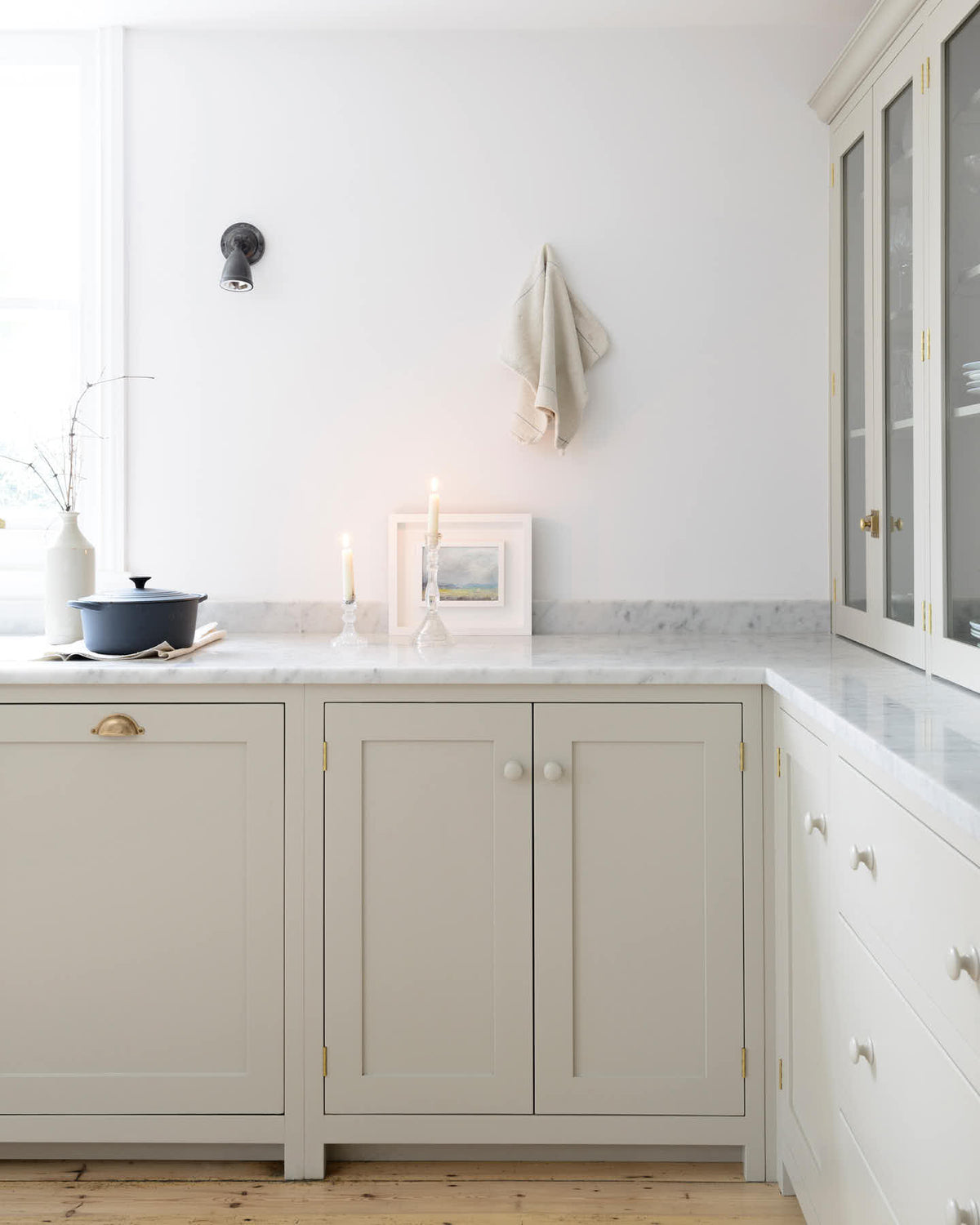 A quiet corner of a simple, mushroom-coloured shaker kitchen with a marble worktop and glazed cabinets peeking around the edge.