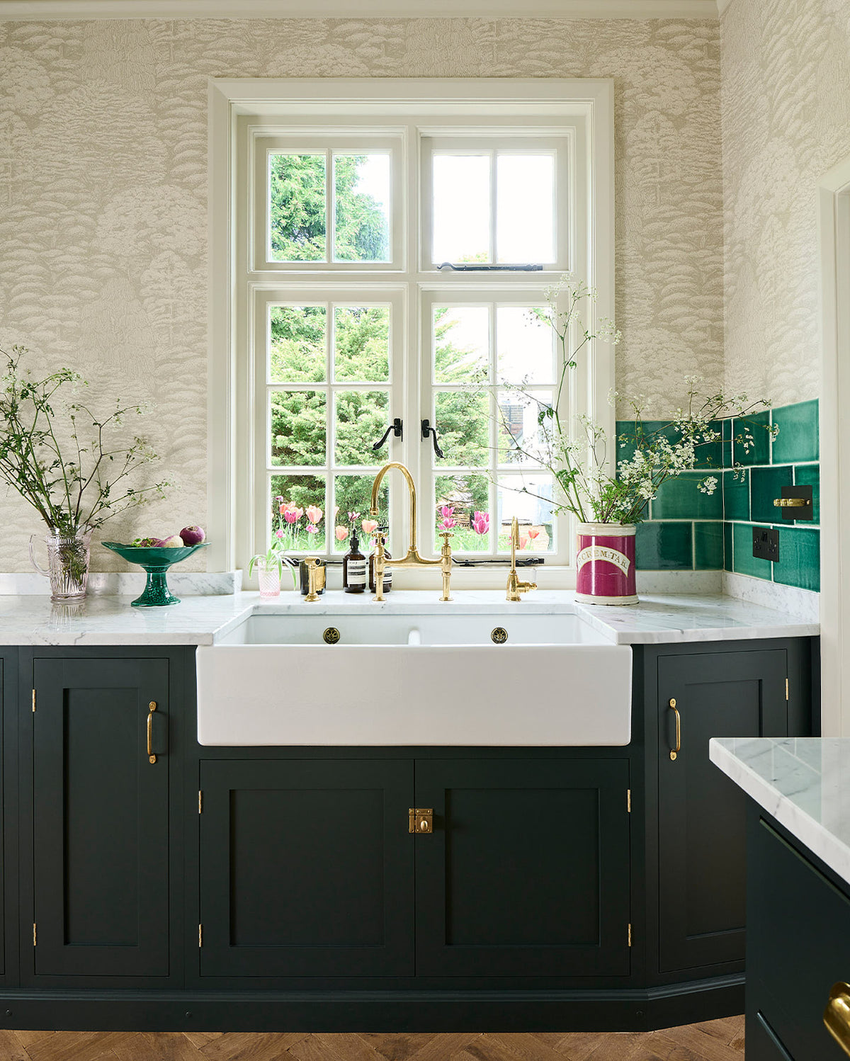 A closer look at the double Belfast sink with an aged brass Ionian tap in the Bakehouse Green shaker kitchen’s sink run, featuring Carrara marble worktop. At the nook are the Emerald Green London tiles, which add colour to the off-white, delicately patterned wallpaper.
