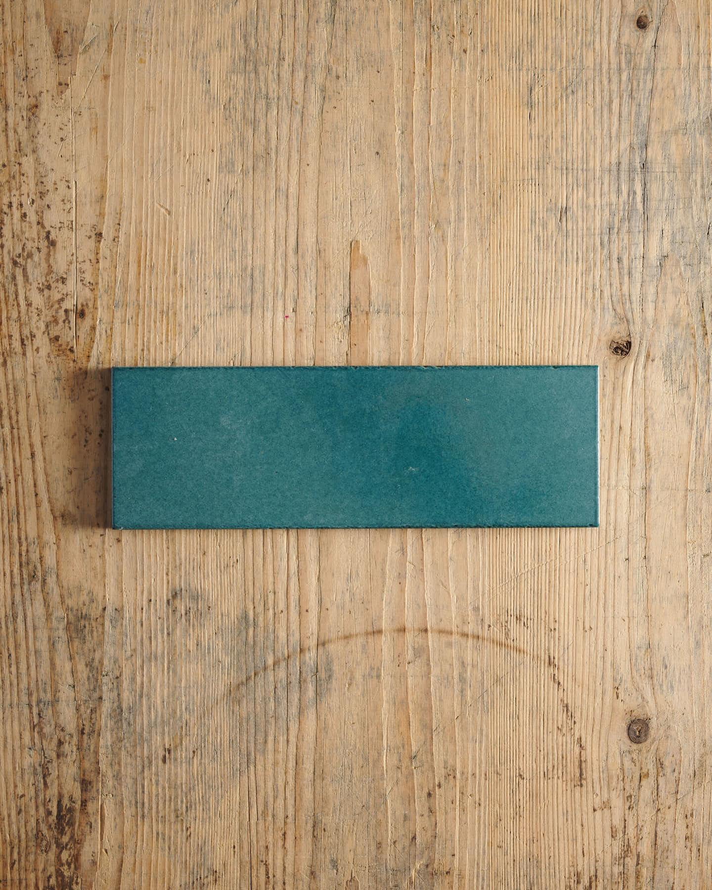 A glossy teal wide metro tile on a rustic wooden surface.