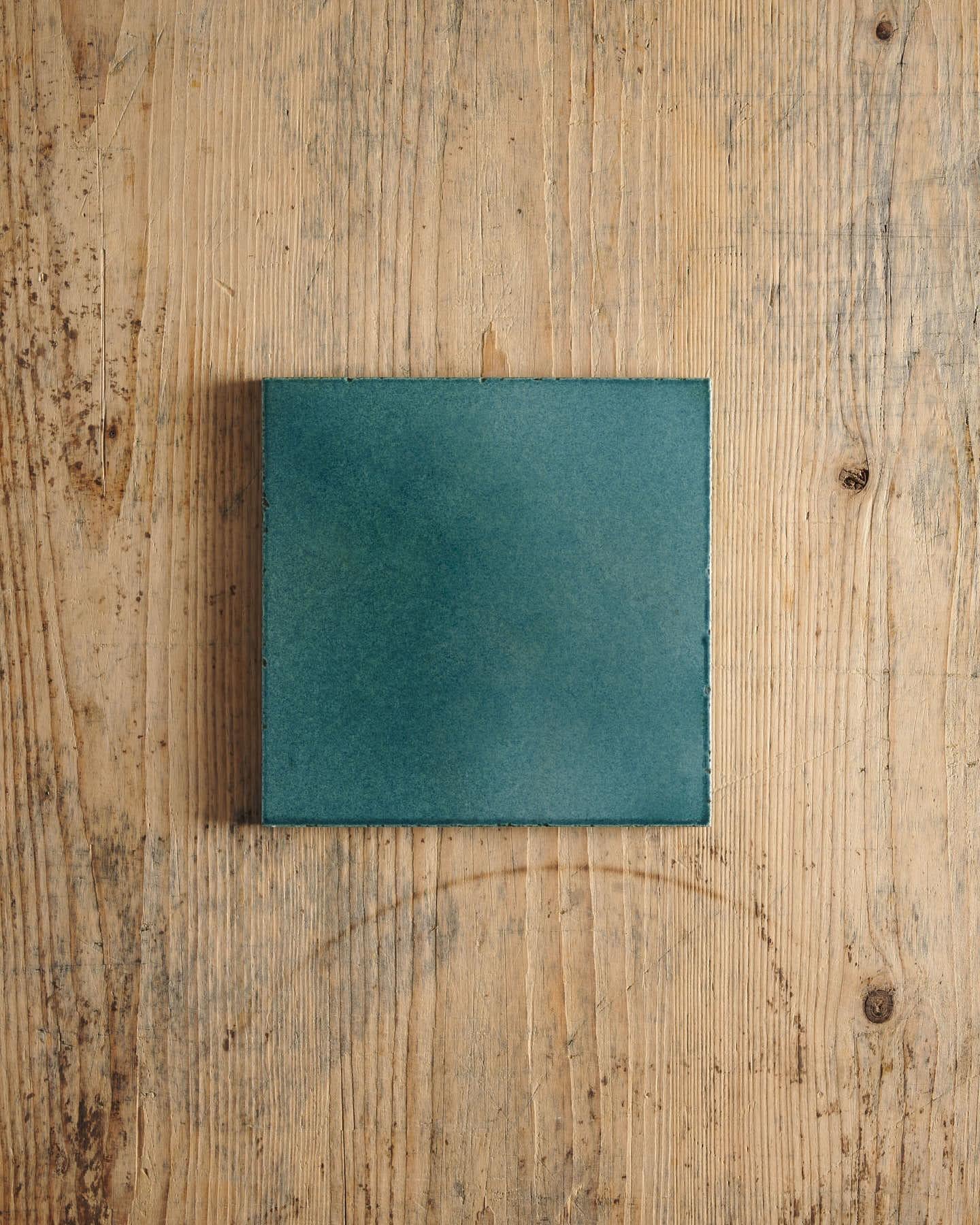 A glossy teal square tile on a rustic wooden surface.