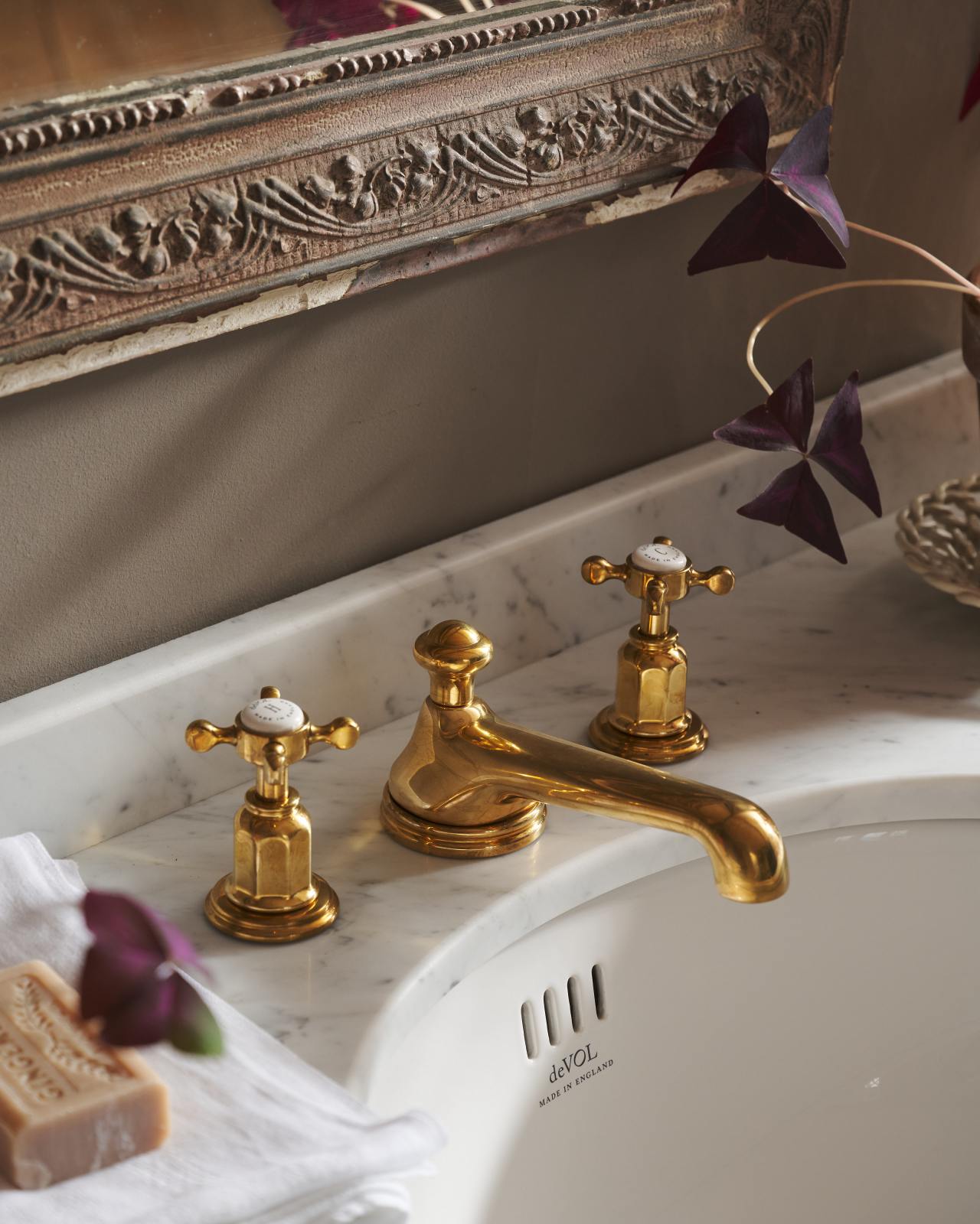 A beautiful aged brass mixer bathroom tap with crosshead handles. The tap has a vintage look and is plumbed into a luxurious marble top, with a small round basin underneath.