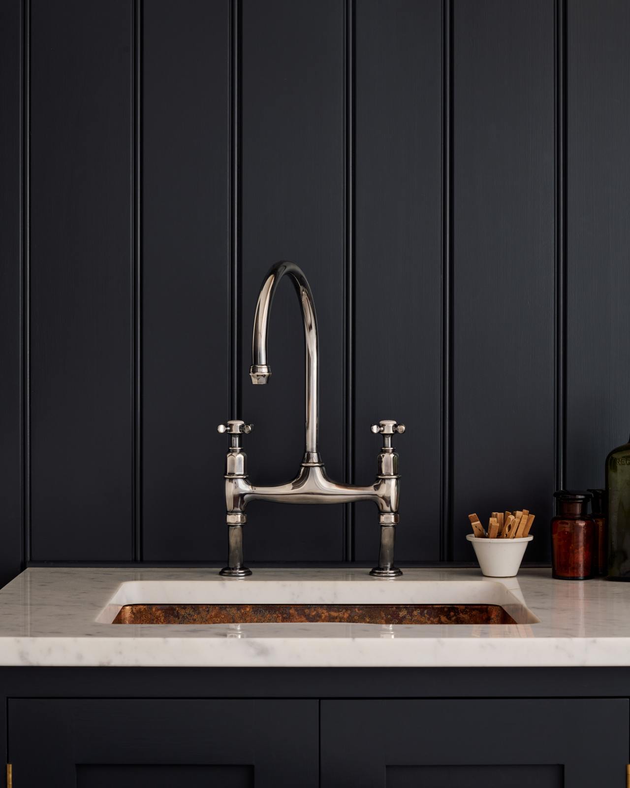 A close-up lifestyle shot of deVOL's new Antique Silver mixer tap, with a swipe to detailed shots of the finish. The style of this tap is quite traditional and it is paired here with a copper sink, polished Carrara marble worktops and a tongue and groove splashback painted in a very dark blue.