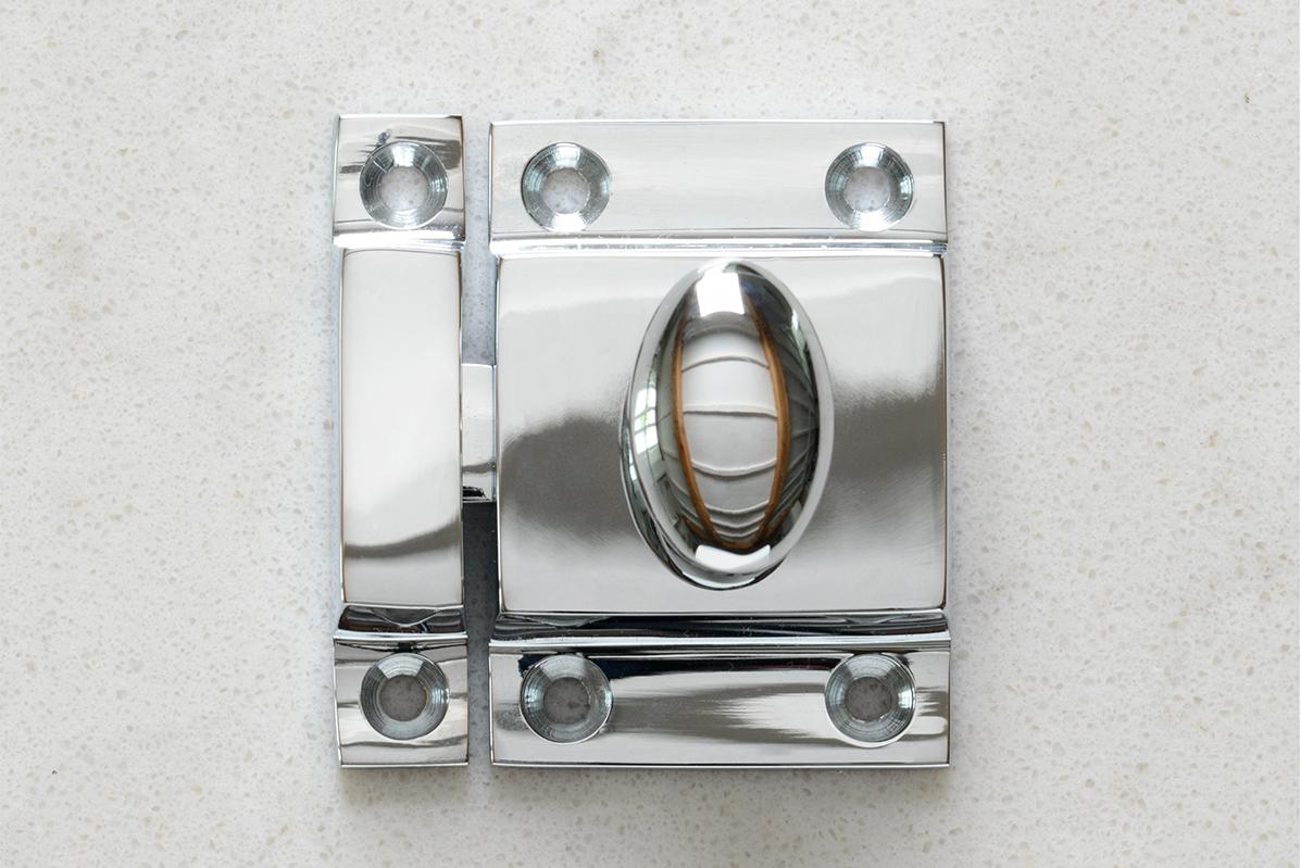 Polished chrome cupboard catch on a light stone surface.