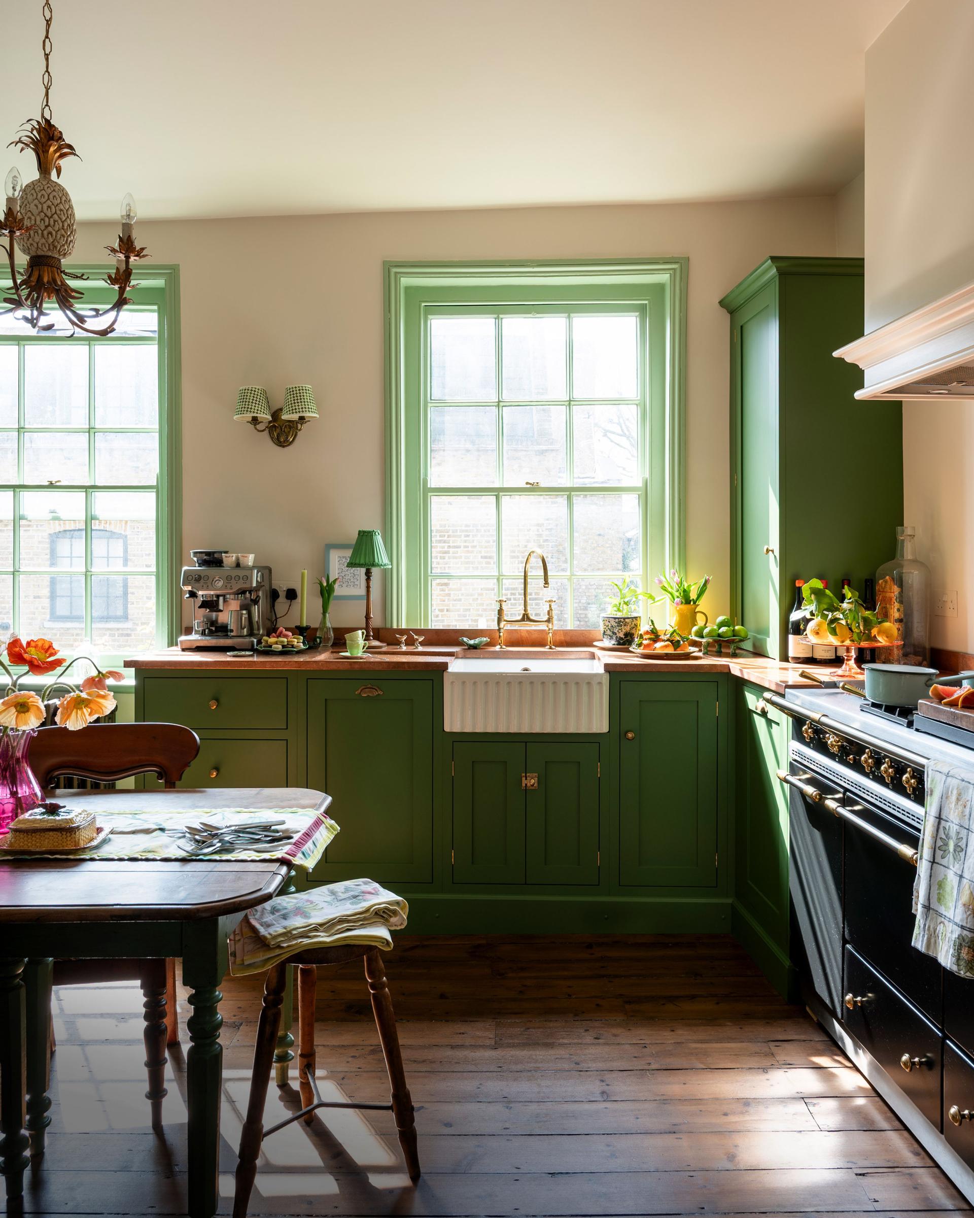 A run of base cabinets and a Belfast sink unit, all painted in a bold pea-green shade, are fitted to the back of this humble kitchen. Further base cupboards, a countertop cupboard and a Lacanche range make up a ‘cooker run’ on the right, creating a simple ‘L’ shaped kitchen. A pair of original sash windows let in a stream of sunshine, and the whole space has a warm, glowy feel.