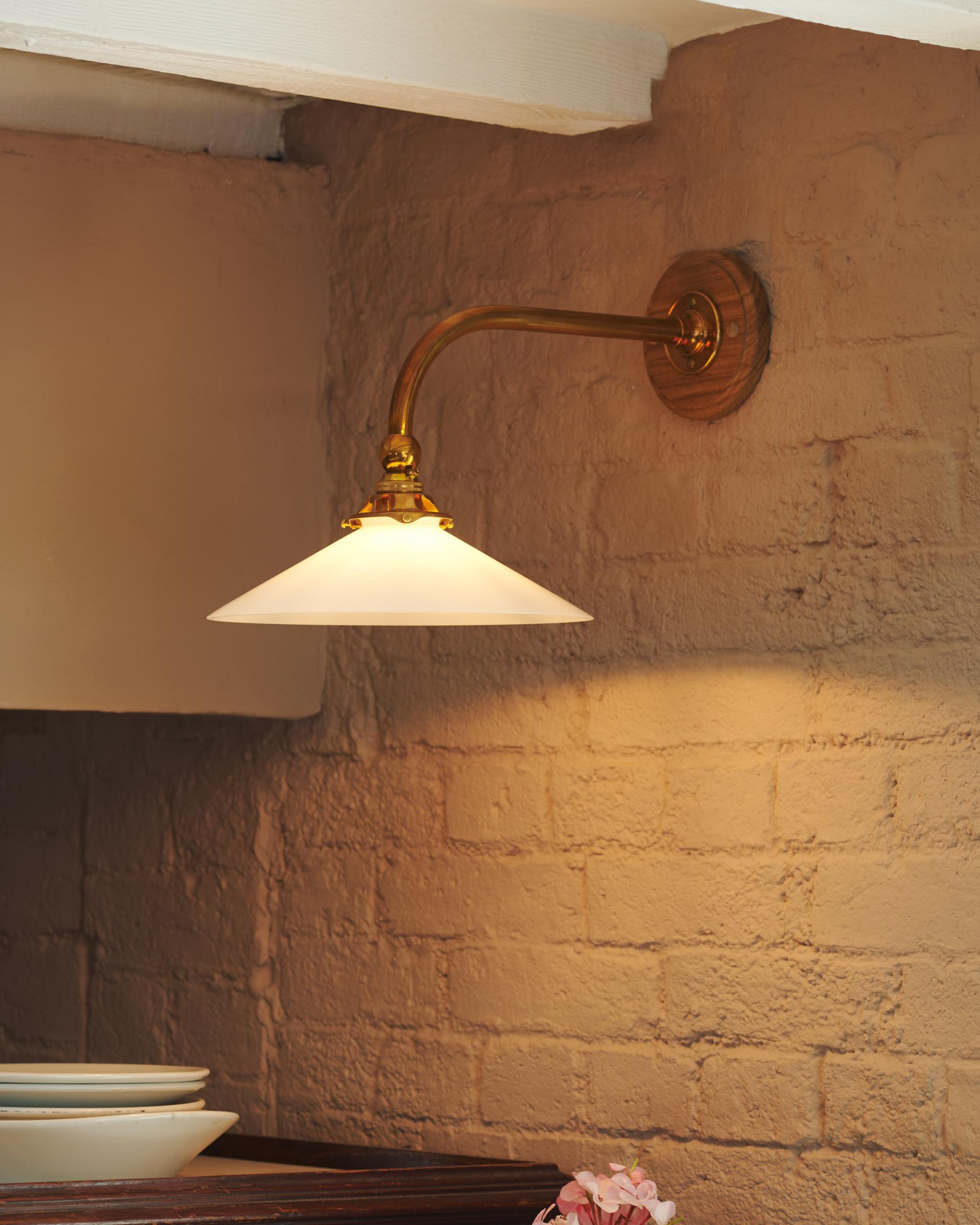 A close up shot of the brass wall mounted task light with details of the brick wall painted in a cream colour.