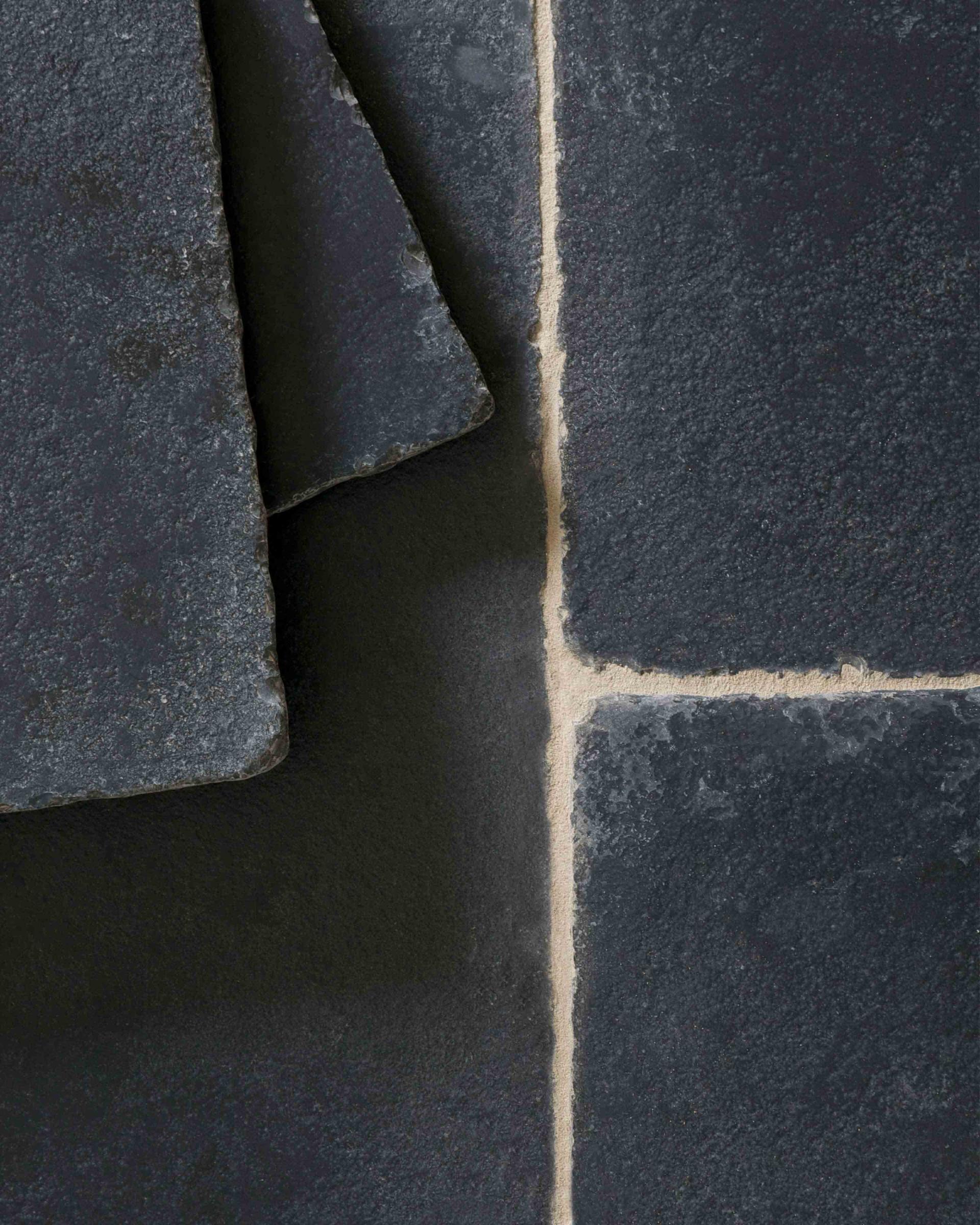 A close-up overhead view of Brushed Charcoal Limestone flooring. Two loose tiles are stacked in the top left corner.