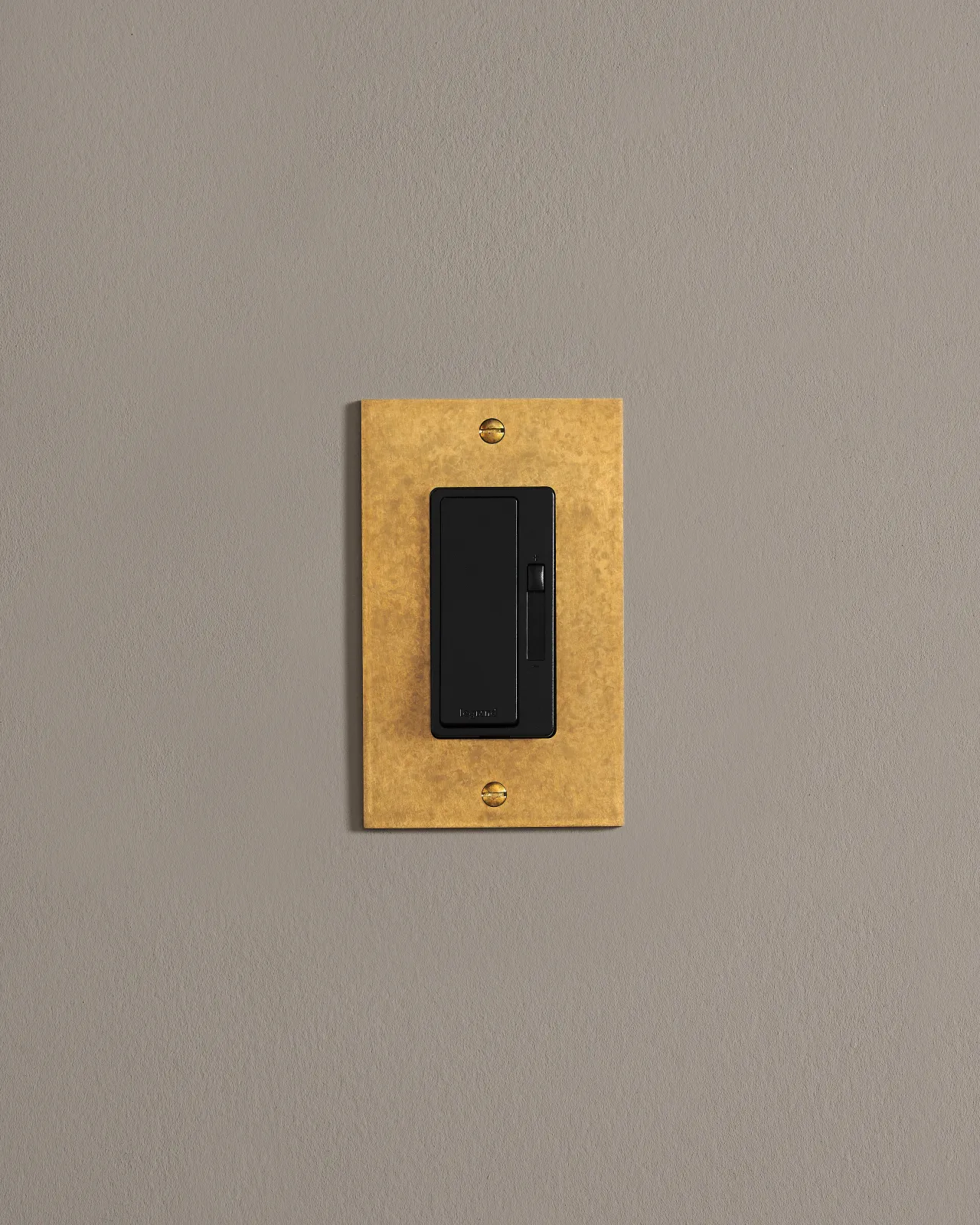 A straight-on view of a 1 gang cover plate in a warm burnished brass finish with a switch module.