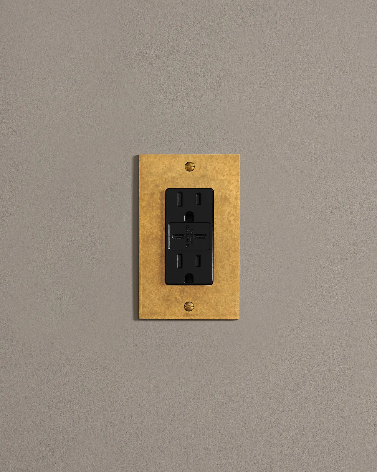 A straight-on view of a 1 gang cover plate in a warm burnished brass finish with a socket module.