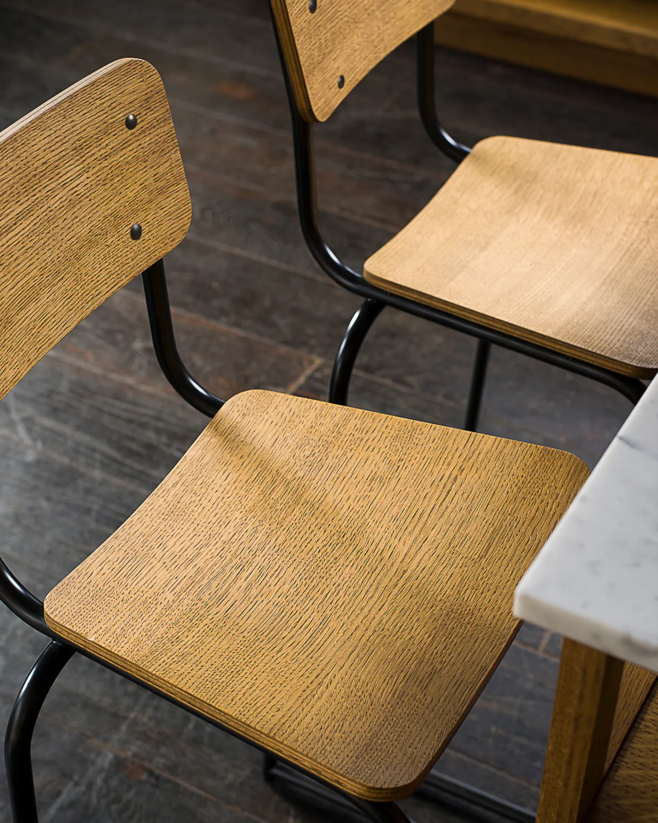 A close-up view of two industrial bar stools with oak veneer plywood seat pans and backrests.