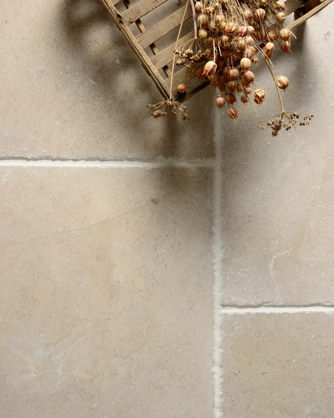 A close-up overhead view of Vintage Bronze Limestone flooring with dried flowers and a small wooden crate.