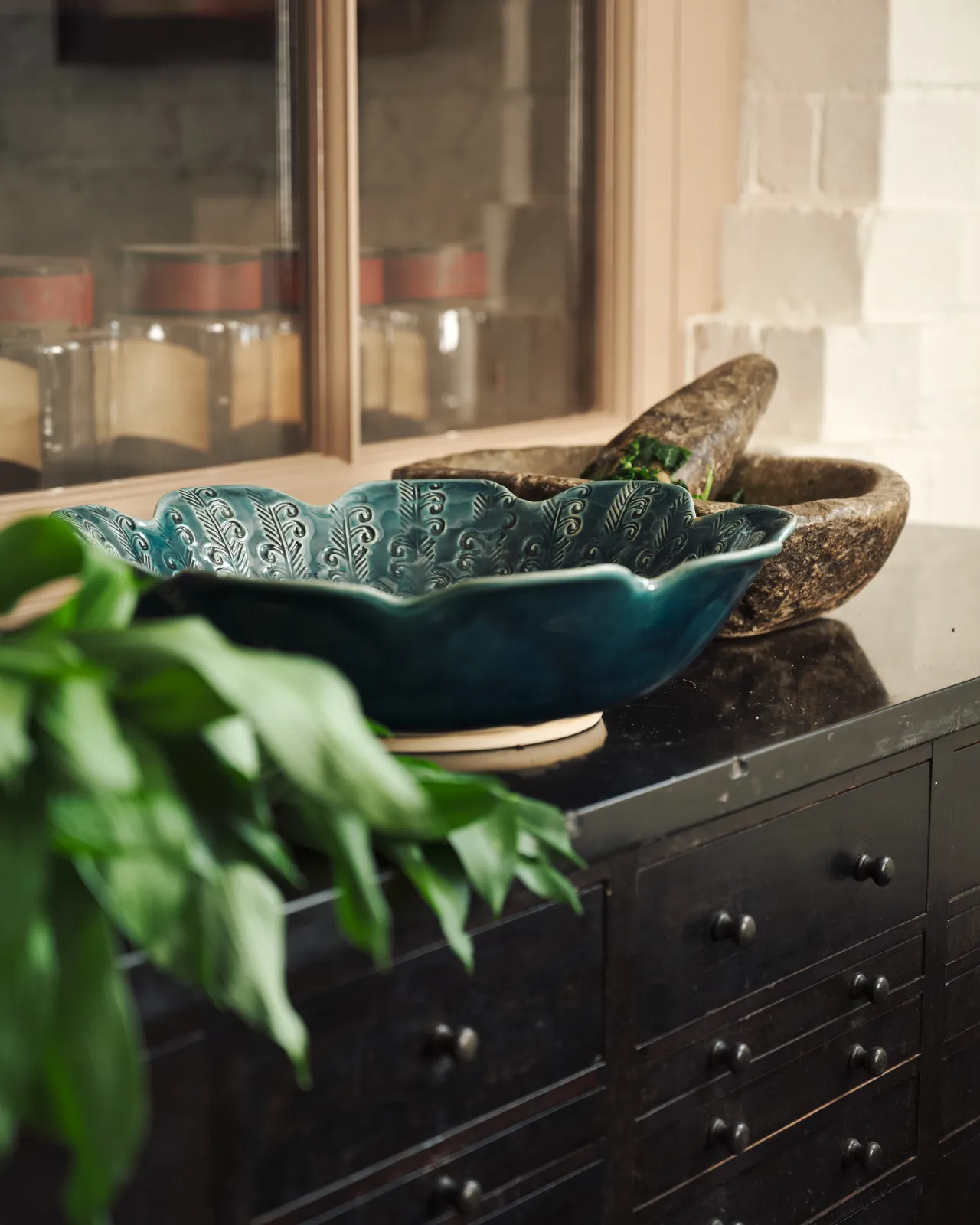 Blue glazed petal-shaped ceramic bowl with embossed pattern, styled with fresh wild garlic on a dark surface.