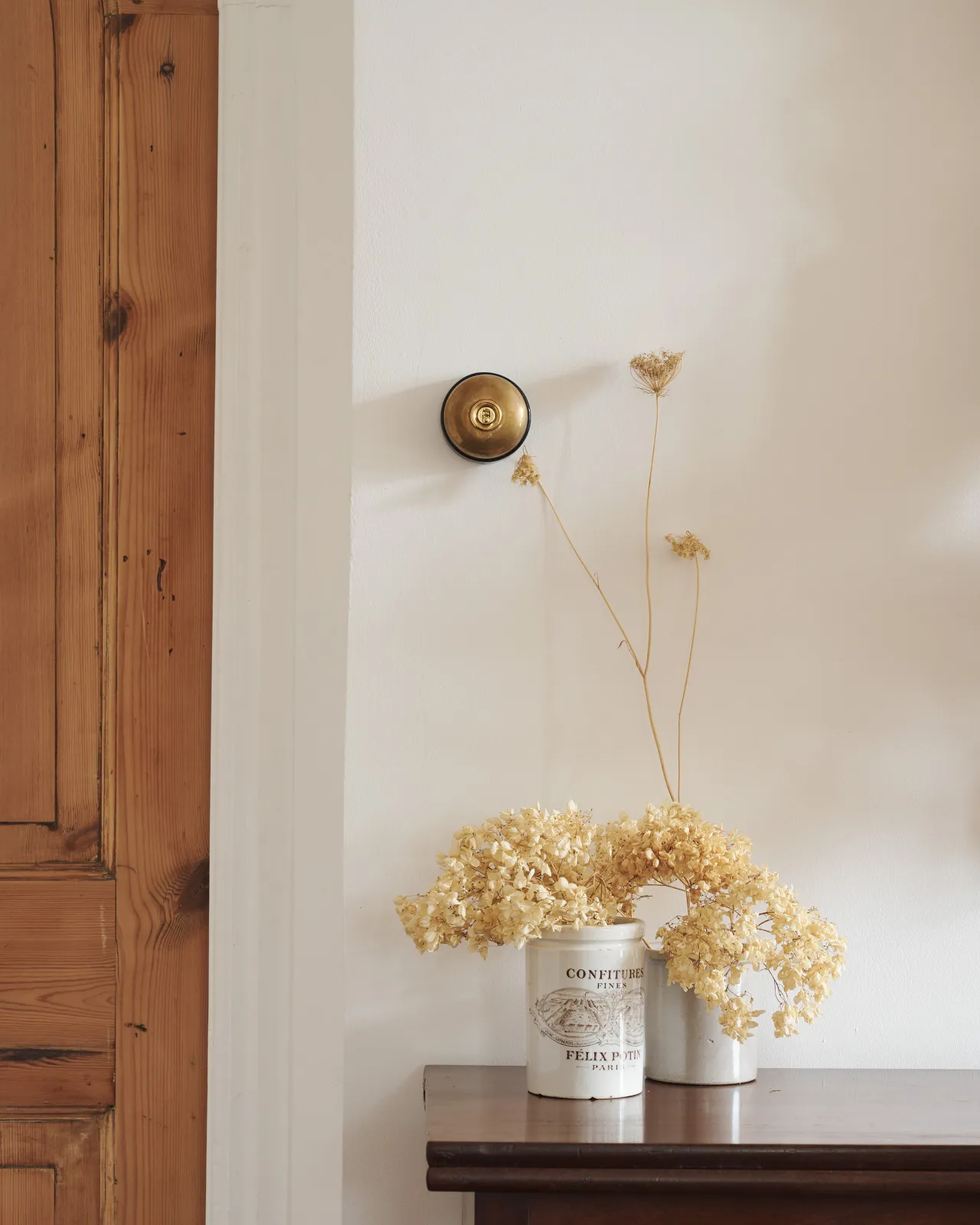A deVOL Dolly Toggle Switch in Heirloom Brass with a black ceramic base. Fitted to a cream painted wall, and styled with creamware pots and dried flowers.
